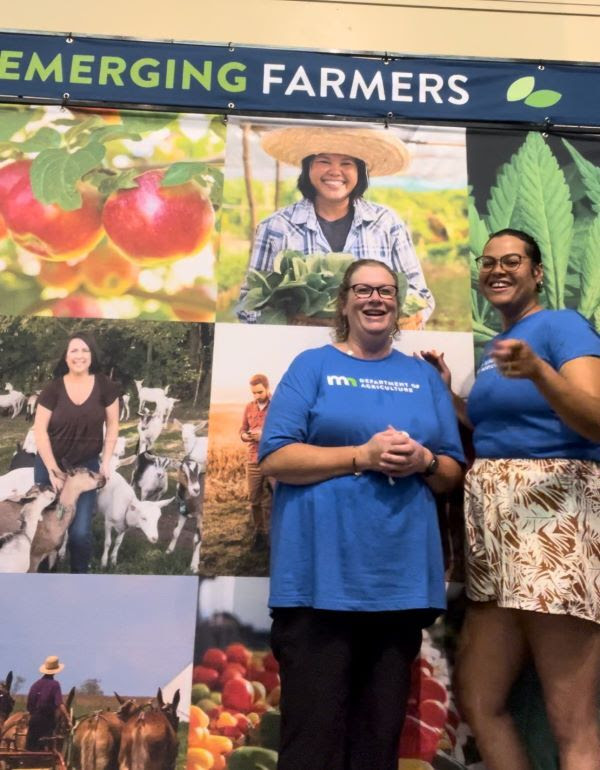 2 OCM staff members smiling in front of emerging farmers poster