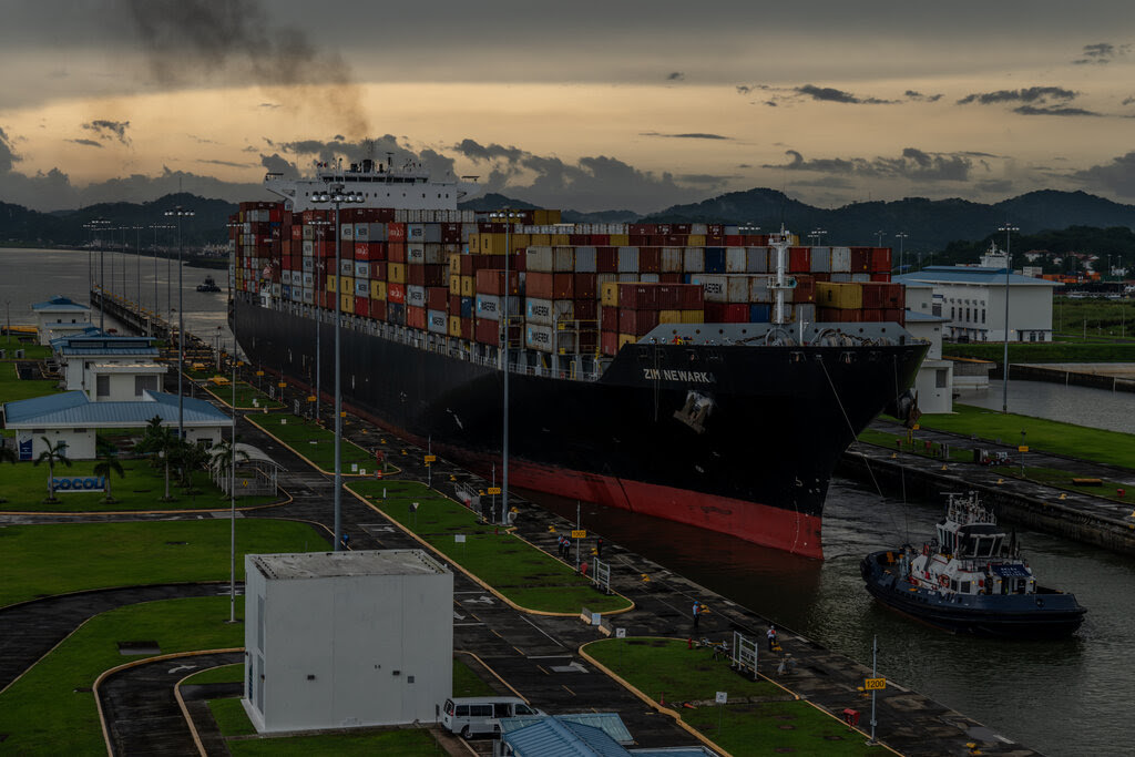 A ship with containers crossing the Panama Canal, with a twilight sky in the distance. 