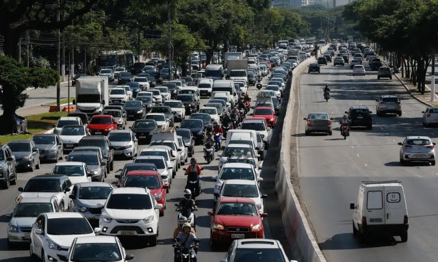 Trânsito em avenida na cidade de São Paulo com motociclistas circulando entre os carros