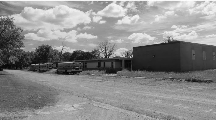 A school building and buses in black and white picture.