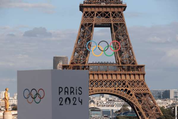 Eiffel Tower decorated with Olympic rings near big block billboard that says 