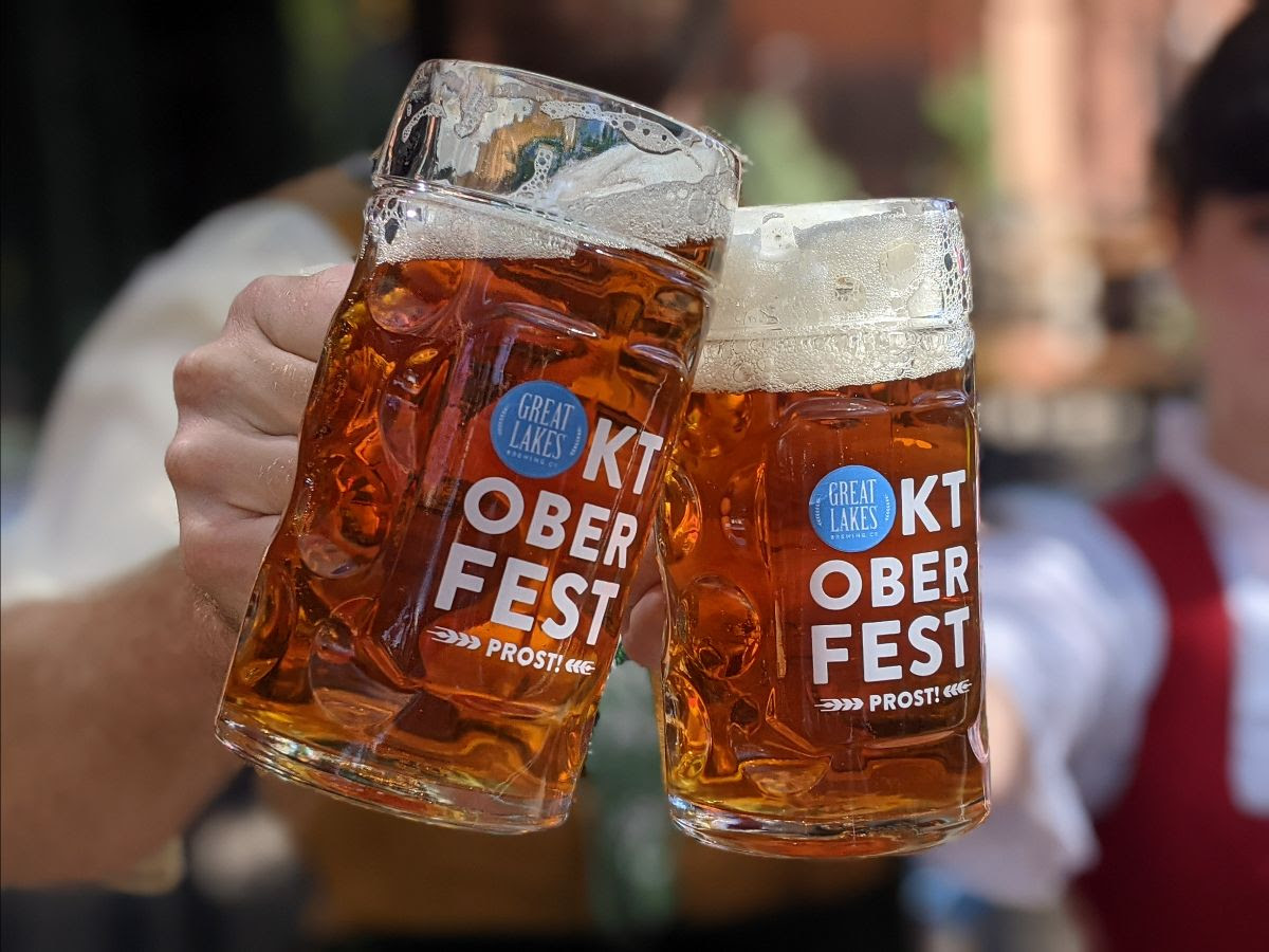 Two people wearing traditional German garb, holding Oktoberfest-branded half liter steins filled with Oktoberfest.