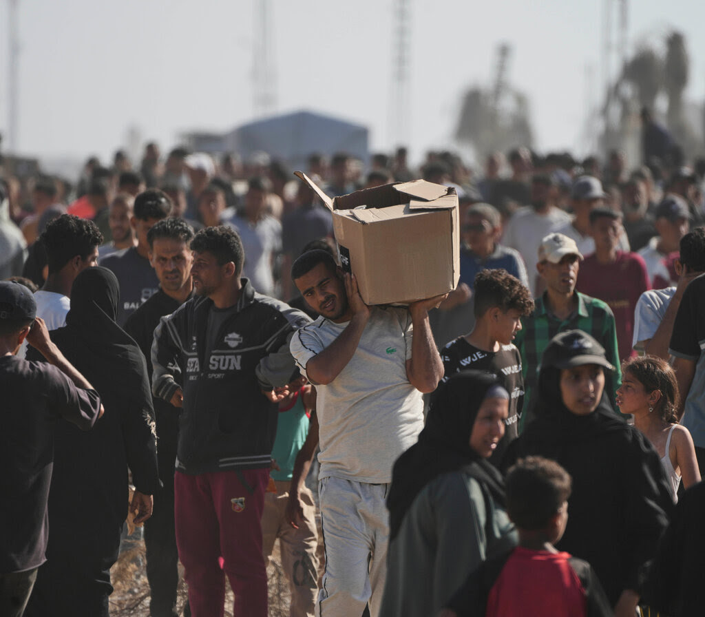 A man at the center of a large crowd carries a cardboard box on one shoulder.