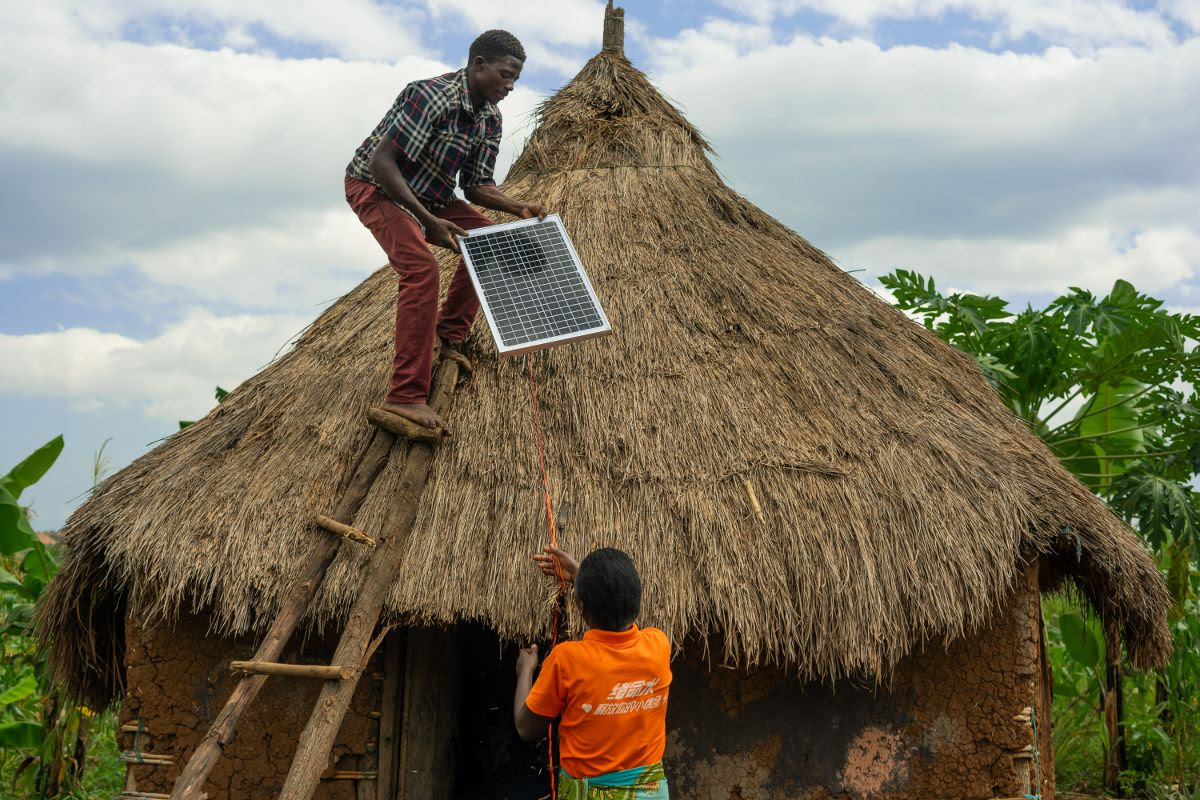 Image depicts members of the local community in Uganda installing solar panels on the roof of a house in their village