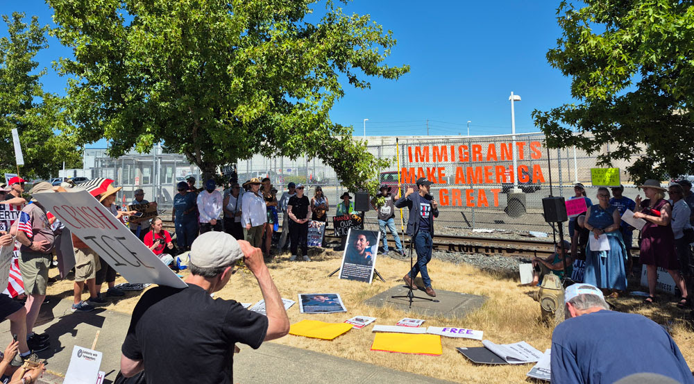Ezra speaks at a protest outside the detention center in Tacoma. A banner reads: Immigrants make America great.