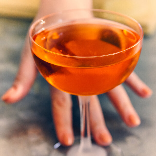 A manicured hand reaches toward a full cocktail glass.