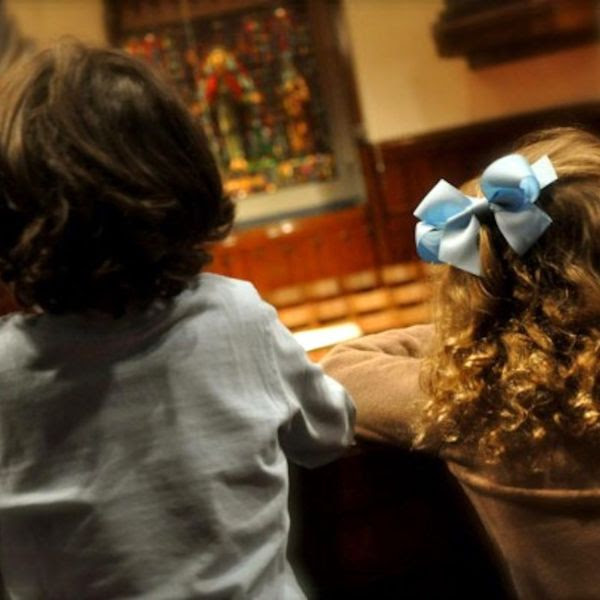 A view from the back and tilted left of two children side by side in a church space