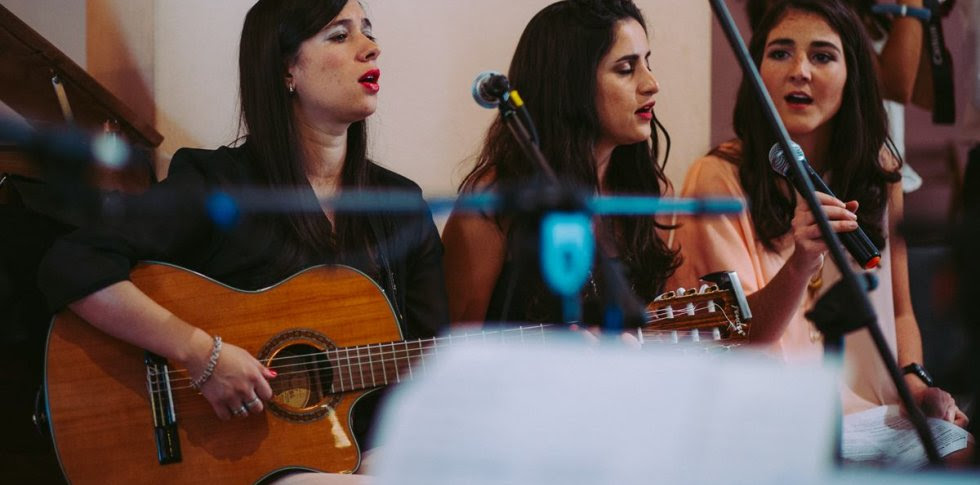 Chicas jóvenes cantando en una iglesia con una guitarra.