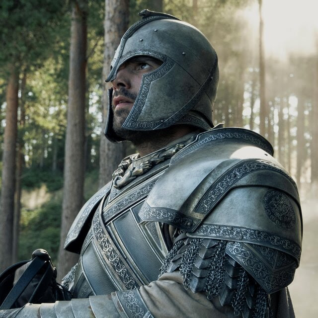 A man in armor in a forest looks up