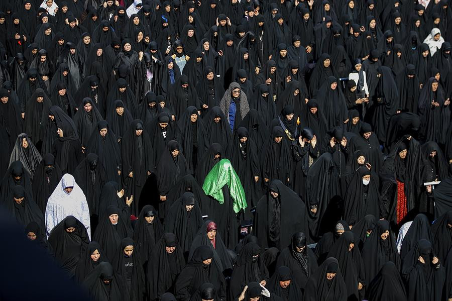 Shiite female pilgrims wearing religious coverings pray. The majority of the women are wearing black or darker colored fabric.