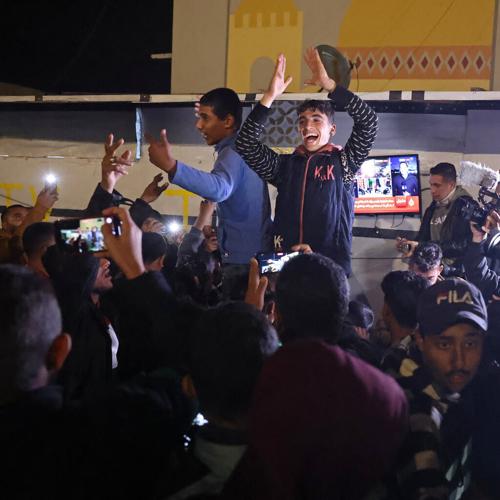 Two people raised above a crowd celebrate by clapping and moving their arms. 