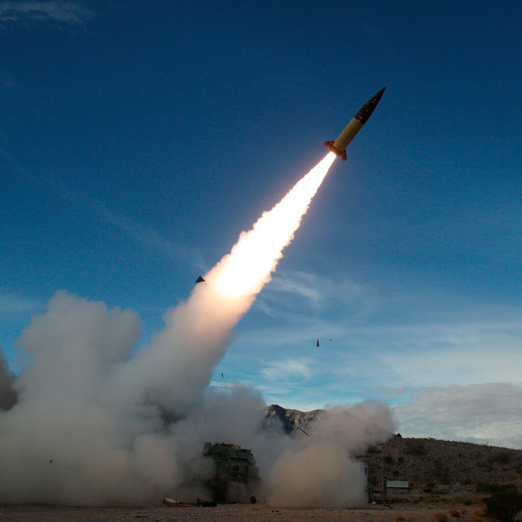 A missile is launched from the ground with a fiery trail across a blue sky.