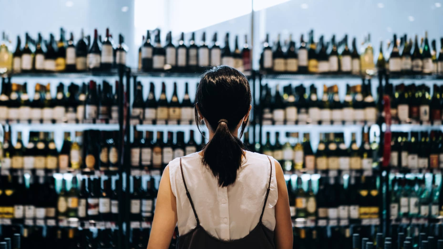 Young Asian woman grocery shopping for wines in a supermarket.