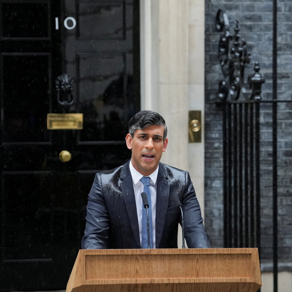 Rishi Sunak standing at a podium outside 10 Downing Street. His suit is wet. 