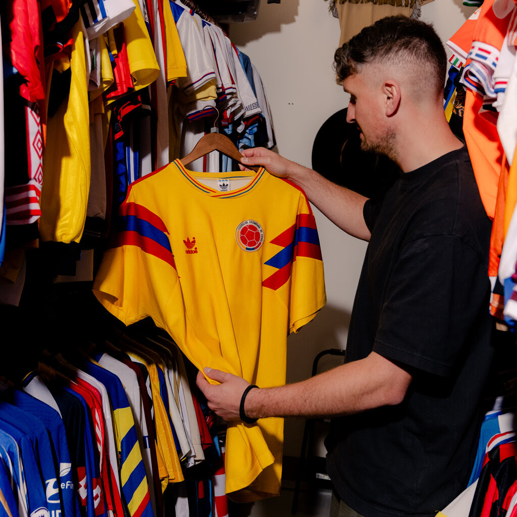 Doug Bierton, dressed in a black T-shirt, holds a bright yellow Romania soccer team jersey from 1990.