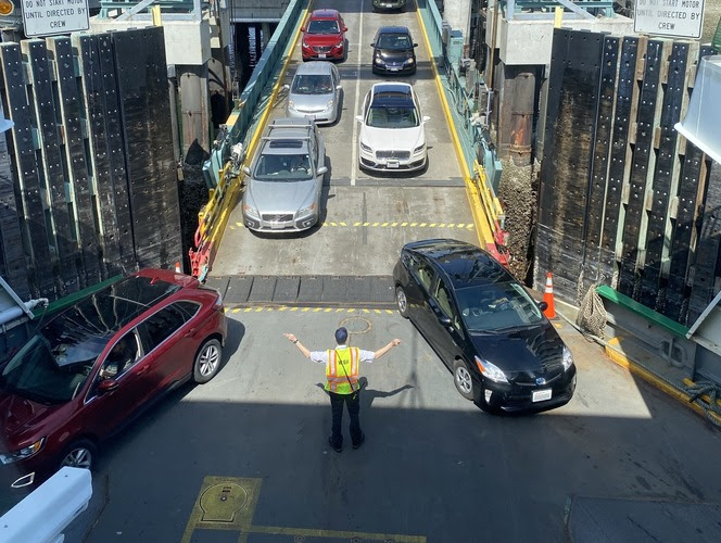 Vehicles boarding a ferry with a crew member in a safety vest directing traffic