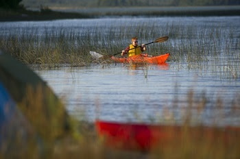 a young man in sunglasses and yellow life jacket paddles an orange kayak at Lime Island Recreation Area in Chippewa County