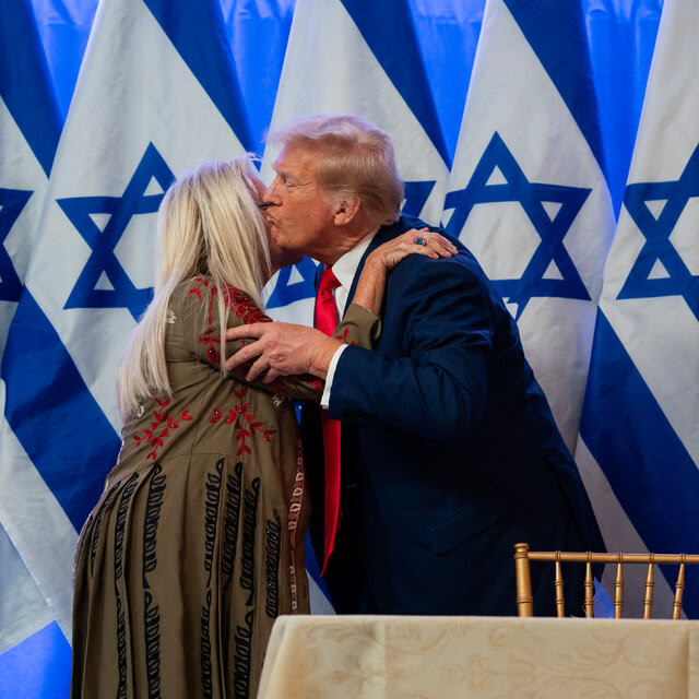 Miriam Adelson, the philanthropist, kisses former President Donald J. Trump in front of a row of Israeli flags.