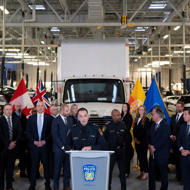 A group of people, some wearing suits, others wearing police uniforms, standing in front of a white truck.