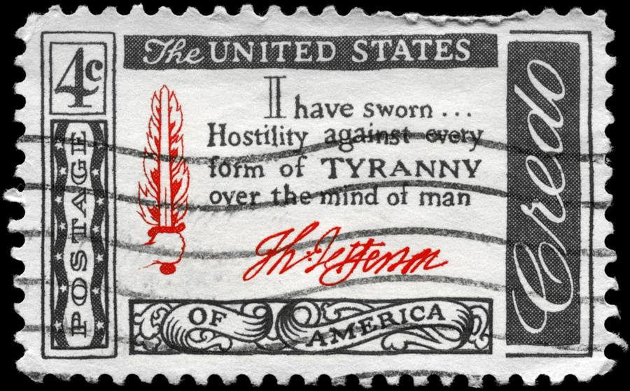 A black and white postage stamp with a small red illustration of a hand holding a flaming sword, and the words 'I have sworn...Hostility against every form of tyranny over the mind of man.'