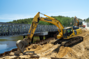 Yellow excavators work on the Chequessett Neck Dike over the Herring River on a sunny day.