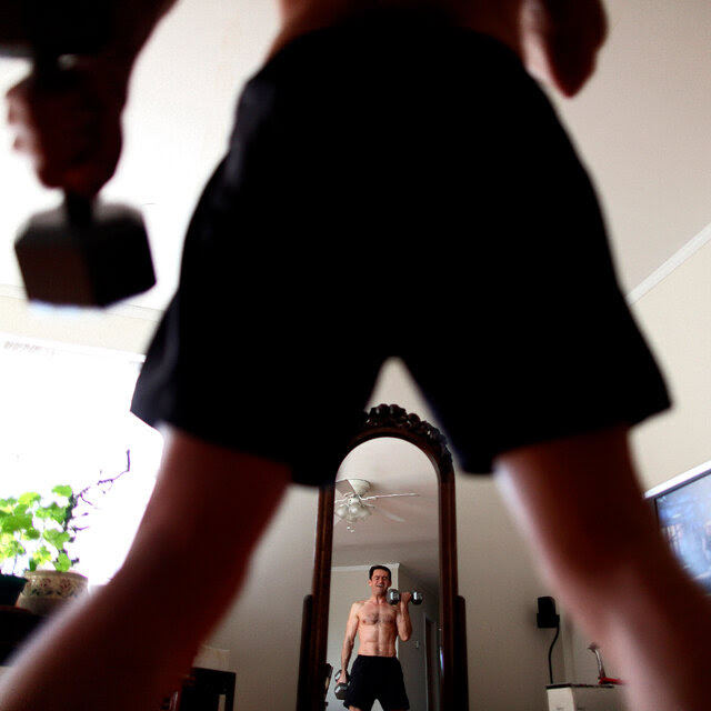 A view from behind of a man lifting weights in front of a mirror.
