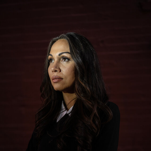 A woman with long hair and business clothes folds her arms as she poses for a photo.