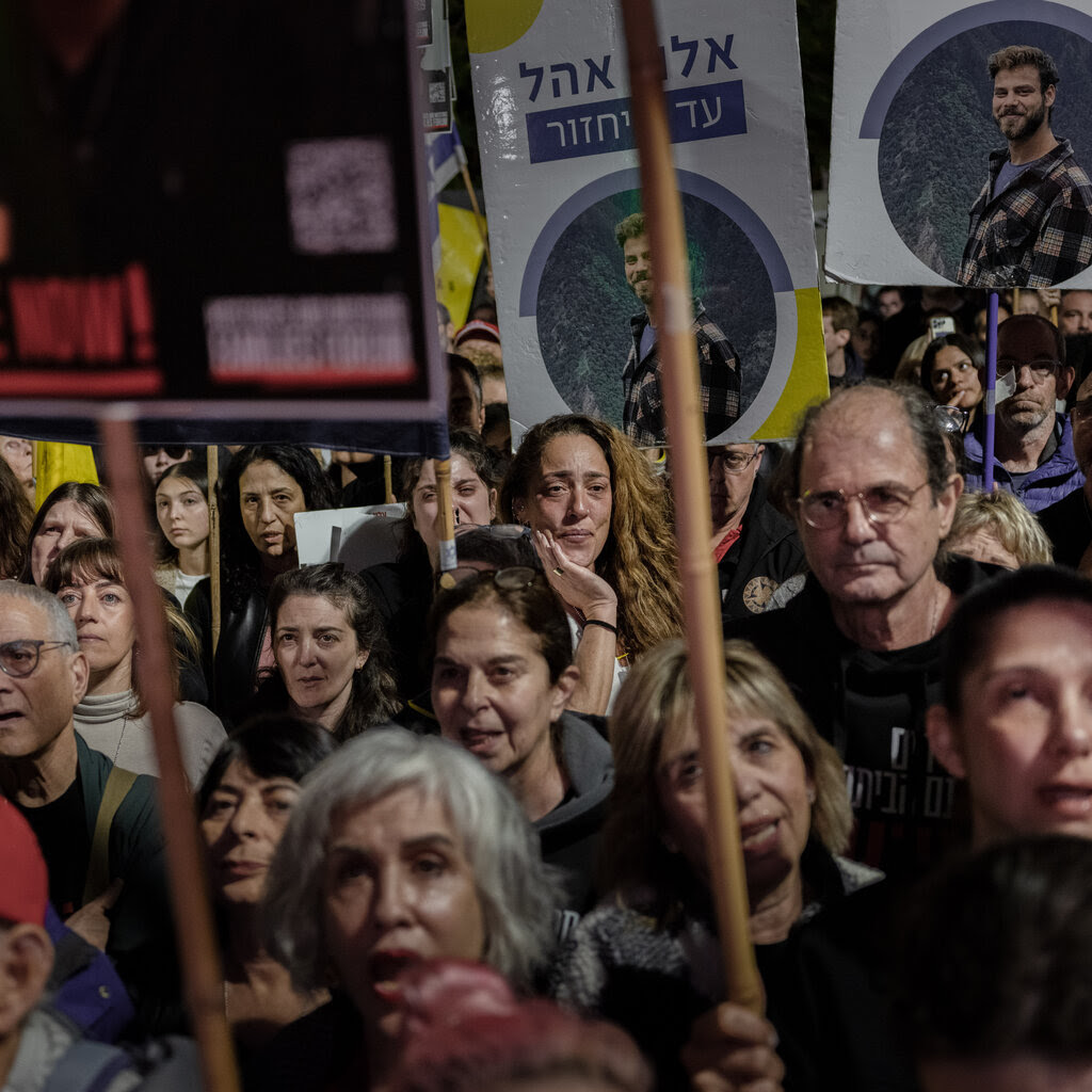 People stand outside at a rally, holding signs. 