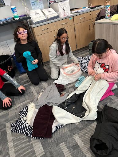 Students sorting clothes on the floor with a teacher in a classroom setting.