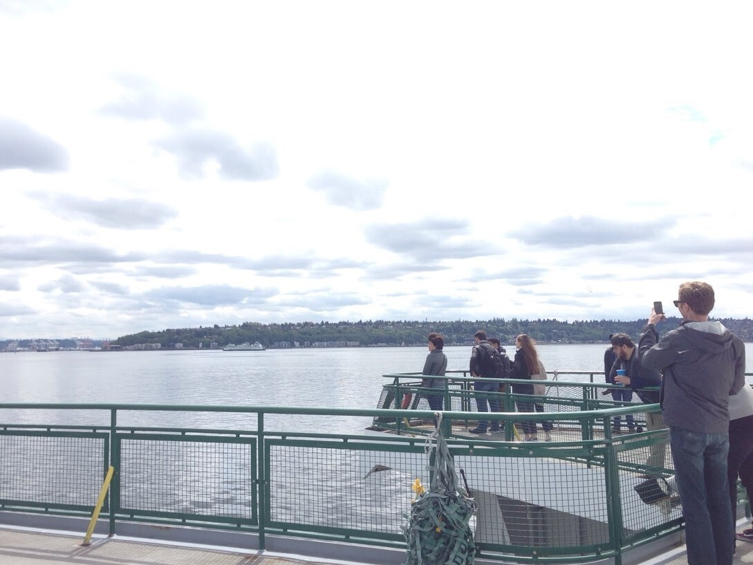 Several people on the outdoor deck of a ferry on a cloudy day