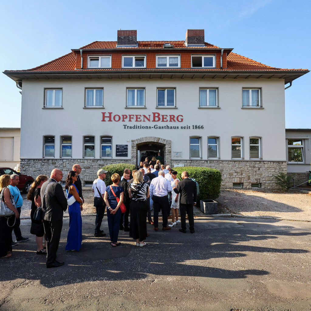 A long lines forms outside a building with the word “HopfenBerg” on it.