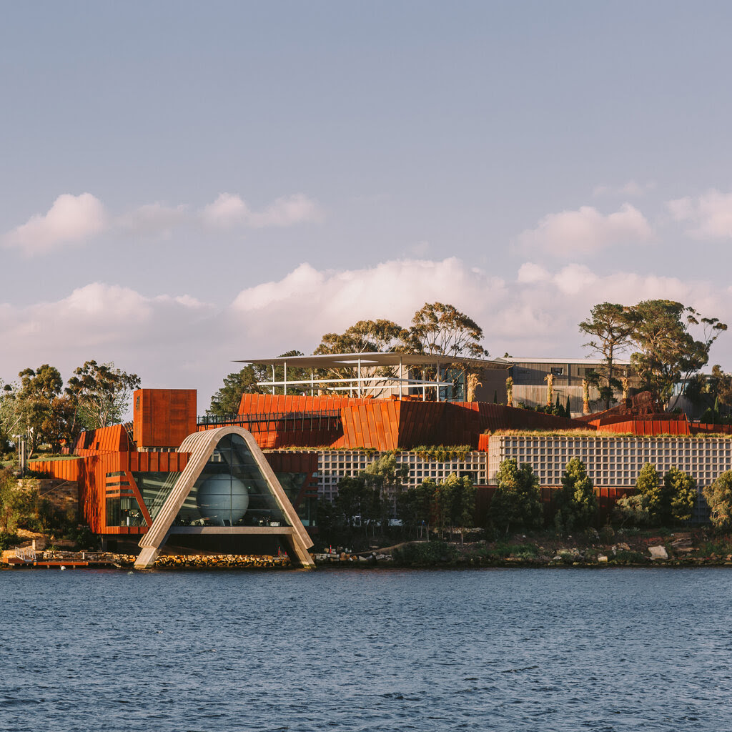 A view of an avant-garde orange and brown museum building from across a body of water.