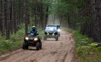 Three ORVs drive safely on the right side of a dirt forest trail.