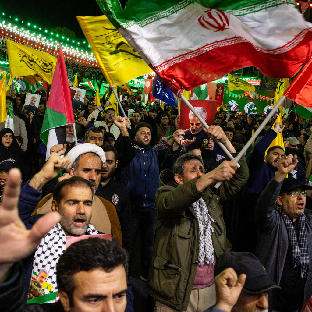 A crowd of people, many with fists in the air, wave Iranian and Palestinian flags.