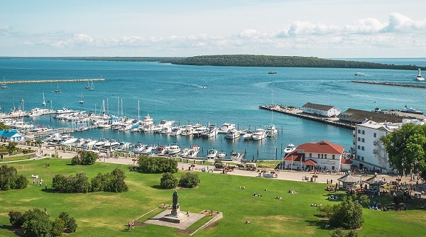 looking down on Mackinac Island State Harbor, dozens of boats in the clear blue water, with white buildings and condos around shoreline