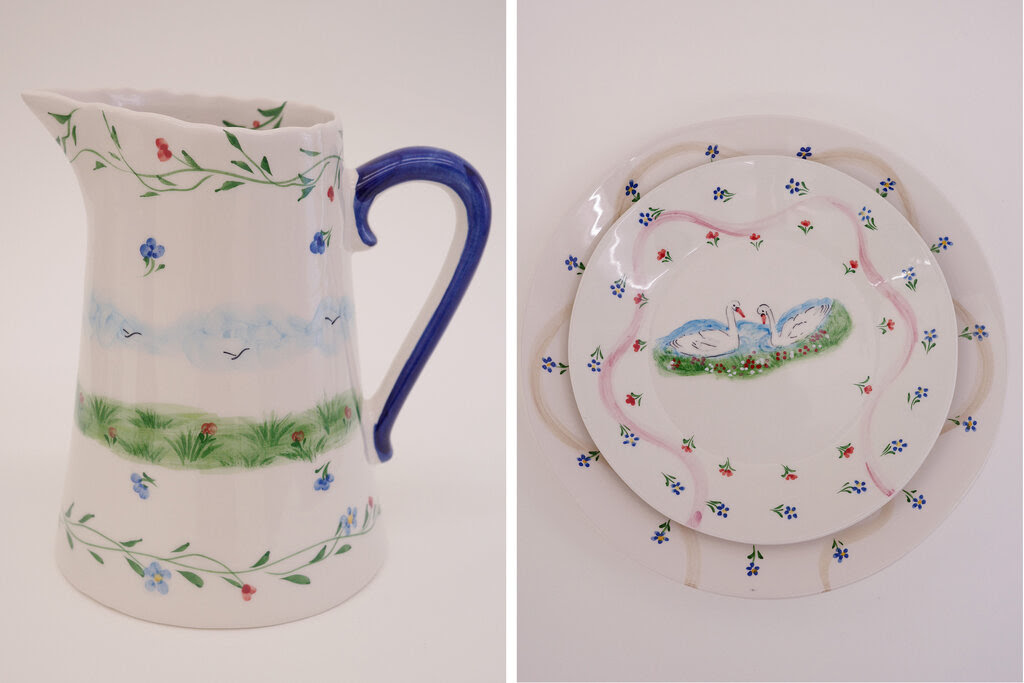 Left, a white pitcher with a blue handle and water-color illustrations of grass, sky and flowers. Right, two plates, the smaller of which has a pair of swans painted on its center.600x400