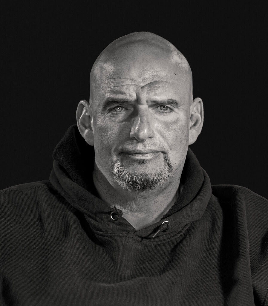 John Fetterman, wearing a hooded sweatshirt, stares into the lens of the camera in a black-and-white photo. 