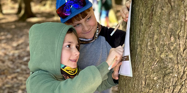 Two children smile as they complete a tree rubbing. 