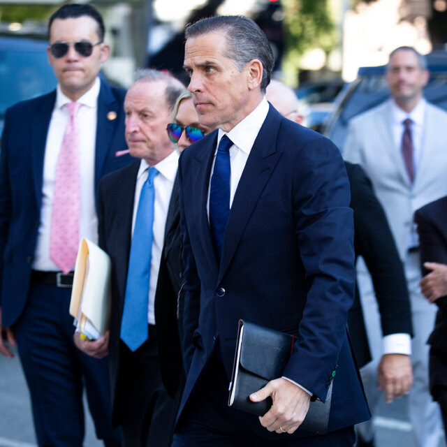 Hunter Biden walking toward a courthouse, surrounded by people in suits.