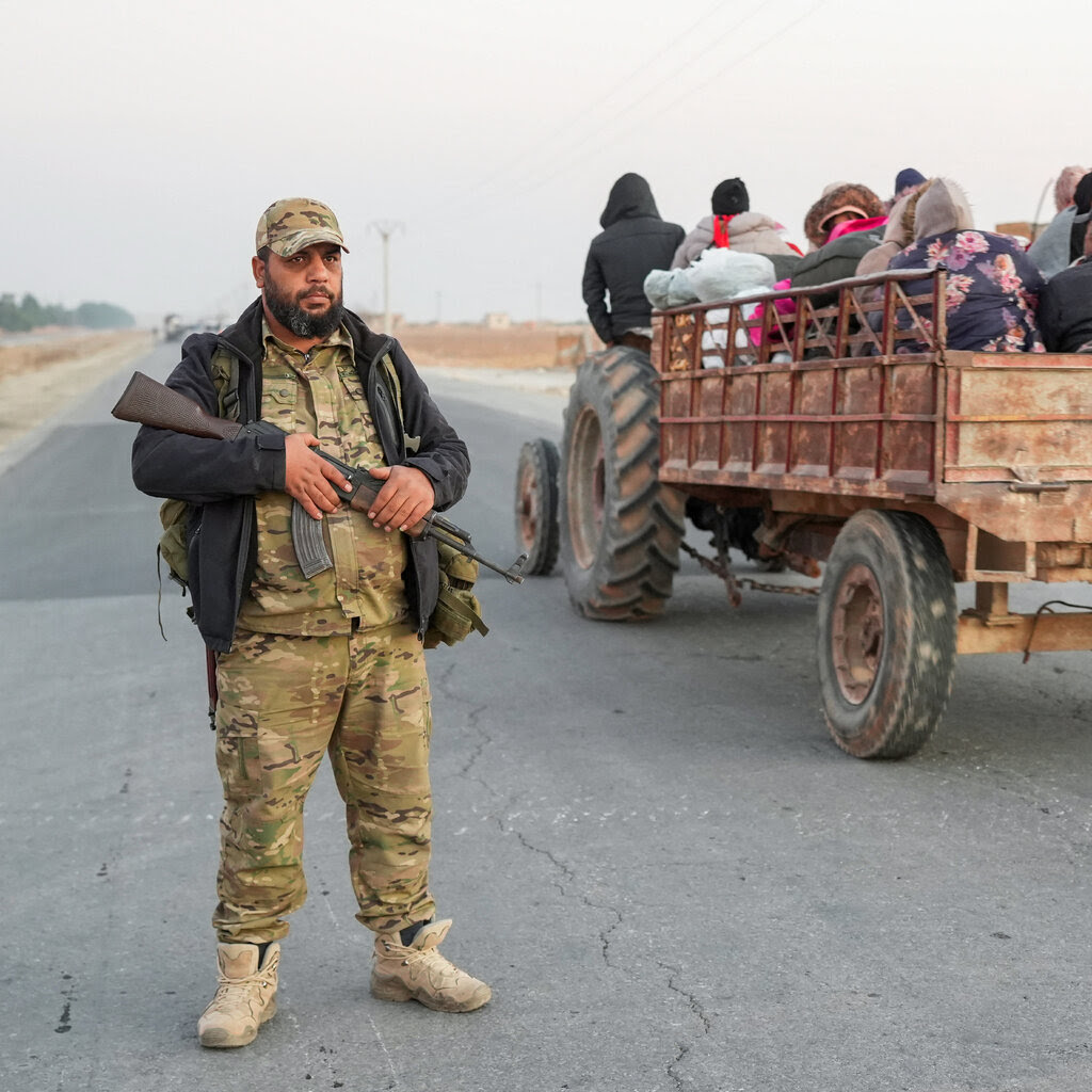 An anti-regime fighter stands on a road as displaced Syrian Kurds drive vehicles loaded with belongings on the Aleppo-Raqqa highway.