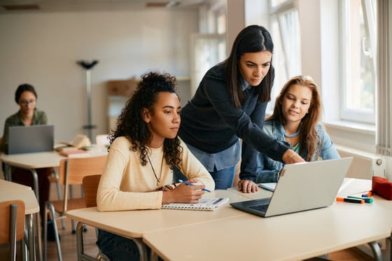 A mentor guides two students on a laptop