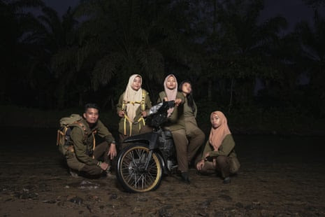 Two female rangers sit on a motorbike with three other rangers sitting around them at night