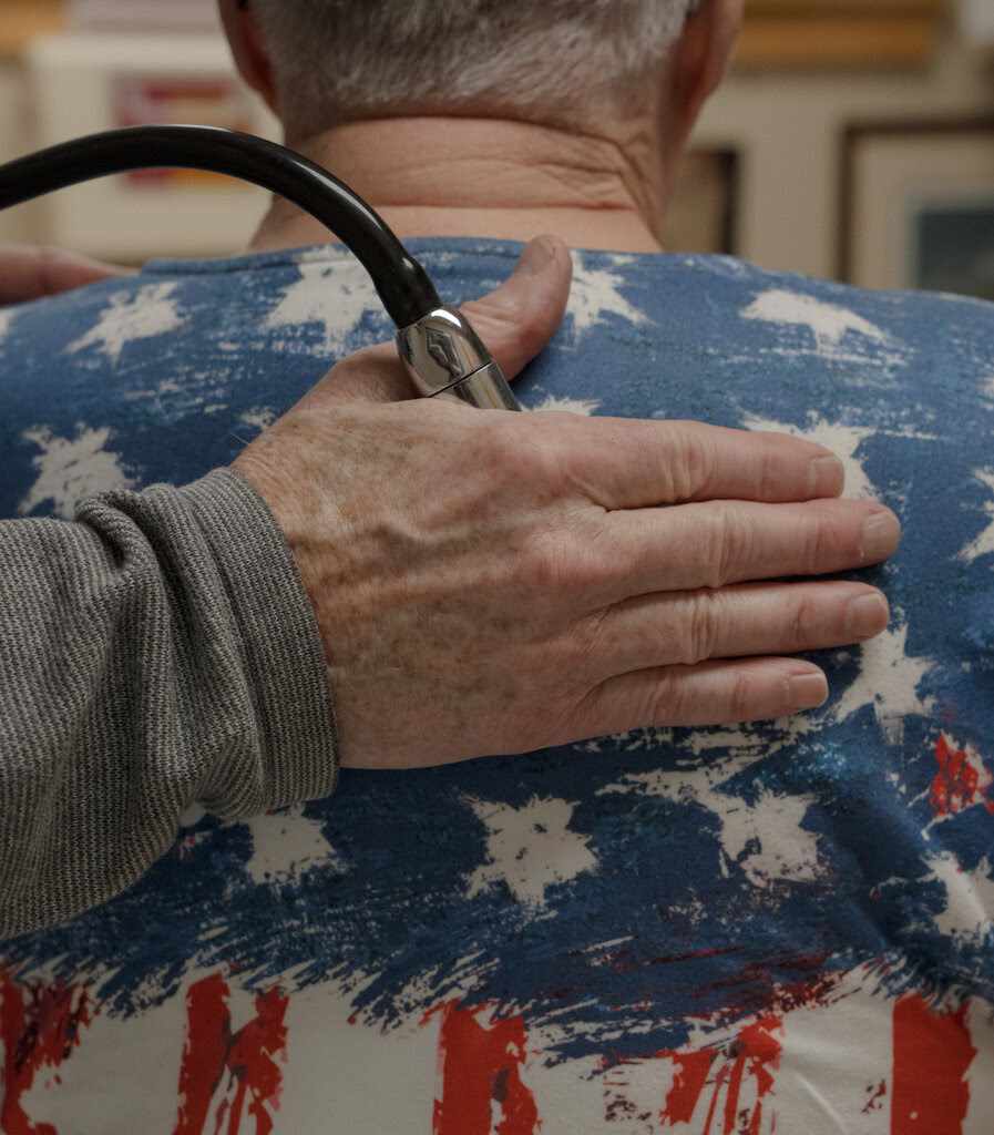 The hand of a doctor holds a stethoscope to a person’s back. 