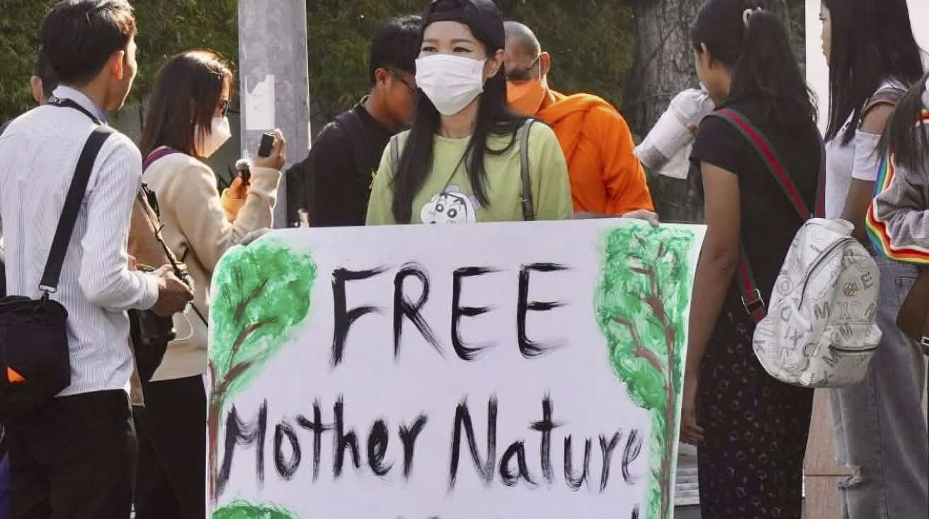 Joven mujer con un gran cartel en el que se lee «¡Liberad a los activistas de la Madre Naturaleza!».