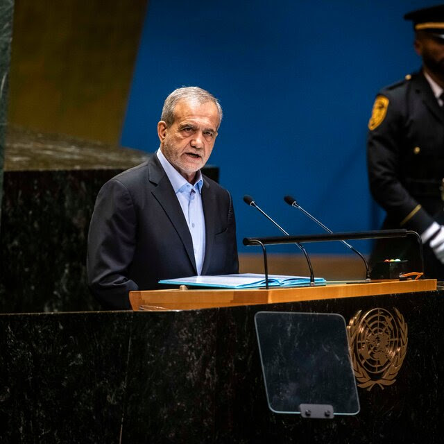 Masoud Pezeshkian, in a suit with an open-necked blue shirt, speaking from a U.N. podium.