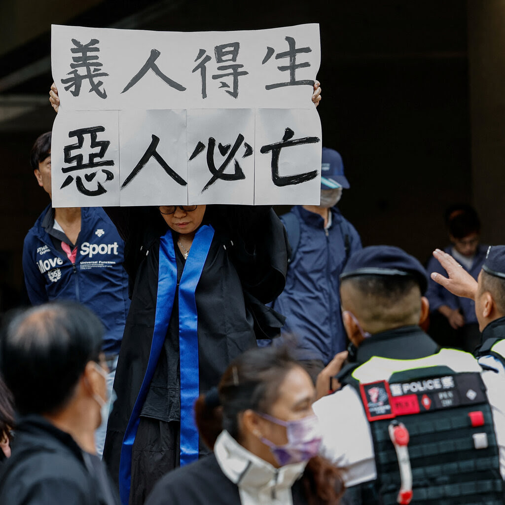 A woman holds up a sign with Chinese characters on it as police officers move toward her to stop her.