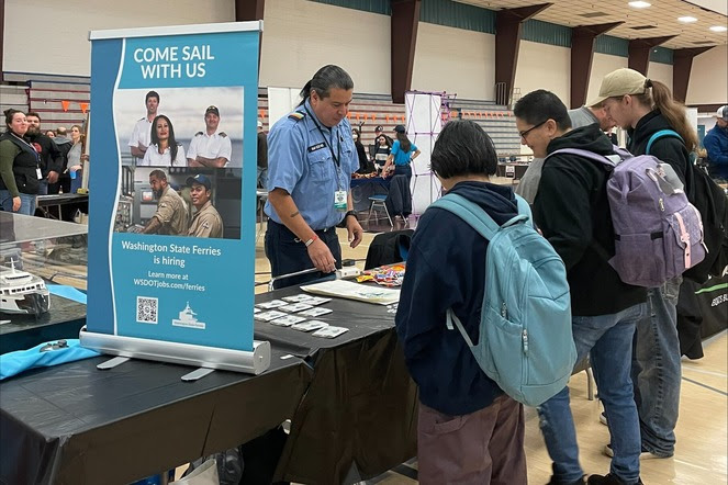 Person in ferry crew uniform behind a table with several high schoolers looking at items on the table