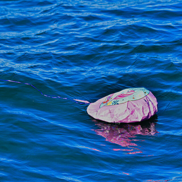 A pink balloon, half-deflated, floats in blue ocean water with a pink ribbon dragging behind it. 