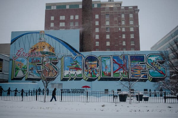 A man walks on a snowy sidewalk in front of a mural reading “Greater Des Moines.”