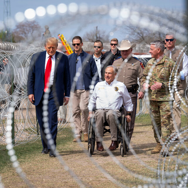 Former President Donald J. Trump and Governor Greg Abbott walking with military members on a path lined with barbed wire.